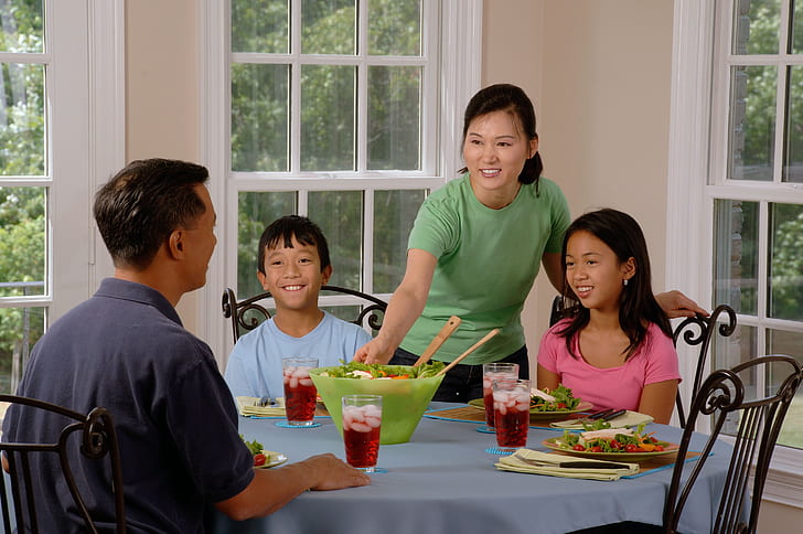 woman standing beside two kids near man sitting on dining table
