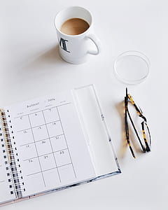 white ceramic mug beside monthly planner notebook