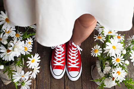 woman wearing white dress and red sneakers standing beside white daisy flowers