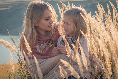blonde haired woman and child sitting on wheat field during daytime