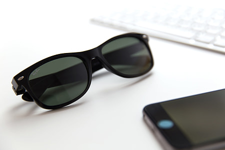 Sunglasses, mobile iPhone smartphone and computer keyboard on a white office desk