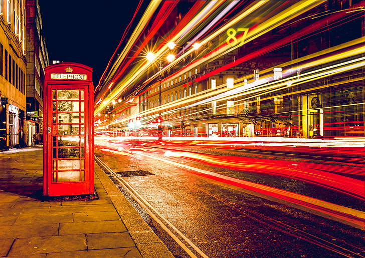 red telephone booth on concrete ground near buildings at nighttime