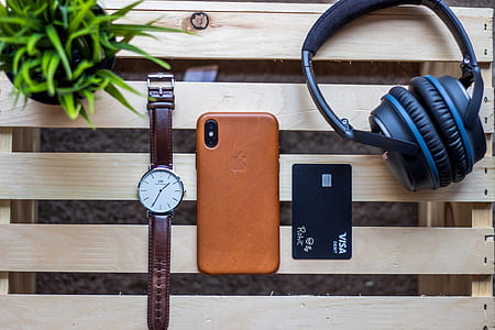 black and blue headphones near space gray iPhone X and brown leather case and round silver-colored analog watch