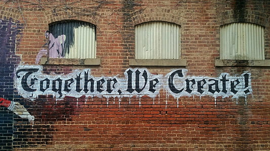 red brick wall with Together We Create paint