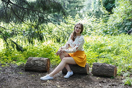 woman wearing white and multicolored long-sleeved shirt and yellow miniskirt outfit sitting on log at daytime
