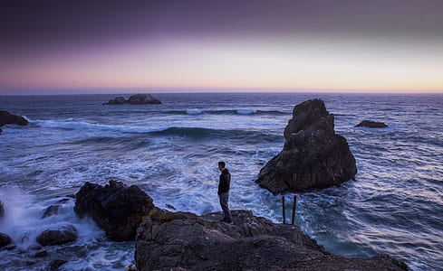 Man in Black Shirt Standing on Rock in Between Sea Water