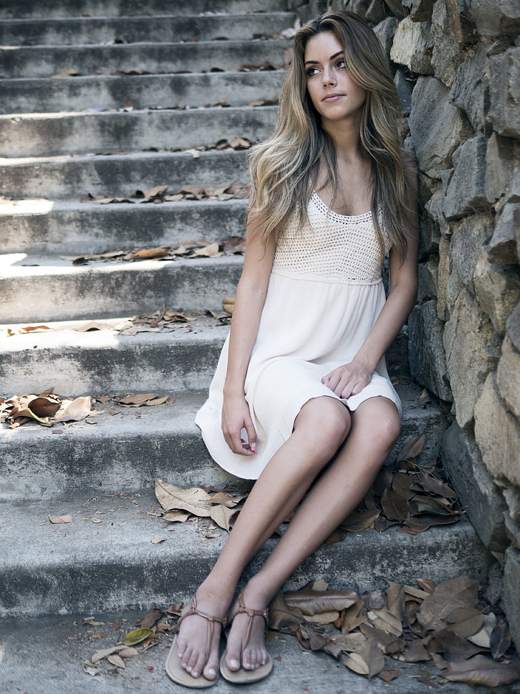 woman wearing white sleeveless dress sitting on concrete step