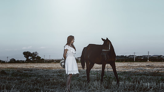 woman wearing white lace dress standing beside black horse