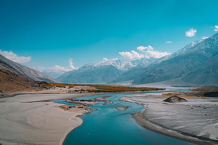 river next to gray sand and mountains under blue sky and white clouds