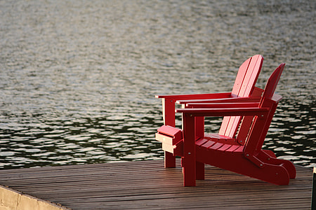 two red wooden armchairs on gray surface beside body of water