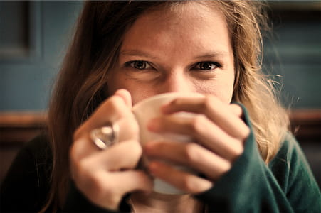 woman wearing green sweater sipping on white ceramic cup