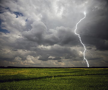 lightning on green field under cloudy sky during daytime