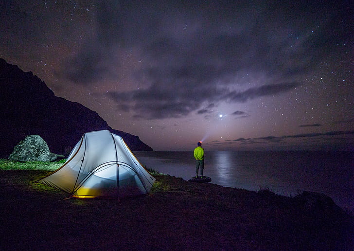 man standing near body of water near lighted dome tent at night