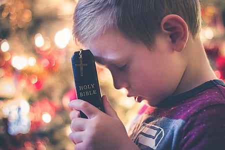 close up photo of boy holding Holy Bible