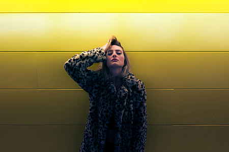 Woman wearing a coat standing by a yellow wall