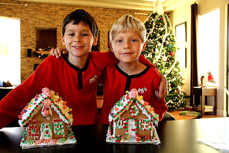 two boys in red-and-black shirts stands in front of cookie house cakes