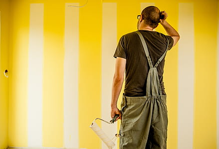 man wearing brown shirt and overalls holding paint roller