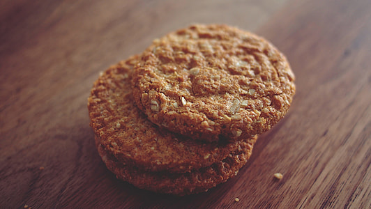 three brown cookies stacked on top of one another placed on brown wooden surface