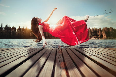 woman in red sleeveless dress floating above brown wooden dock during daytime