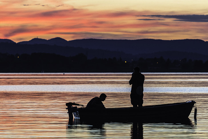 Fishermen in boat at sunrise, silhouettes of people on lake or