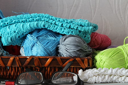 blue, green, and gray yarns on basket near black framed eyeglasses