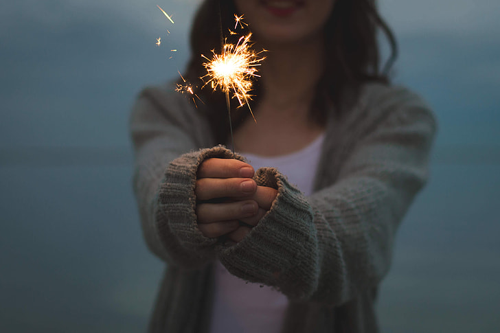 shallow focus photography of woman in gray knitted cardigan holding fireworks