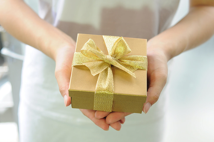 person holding gold box with ribbon