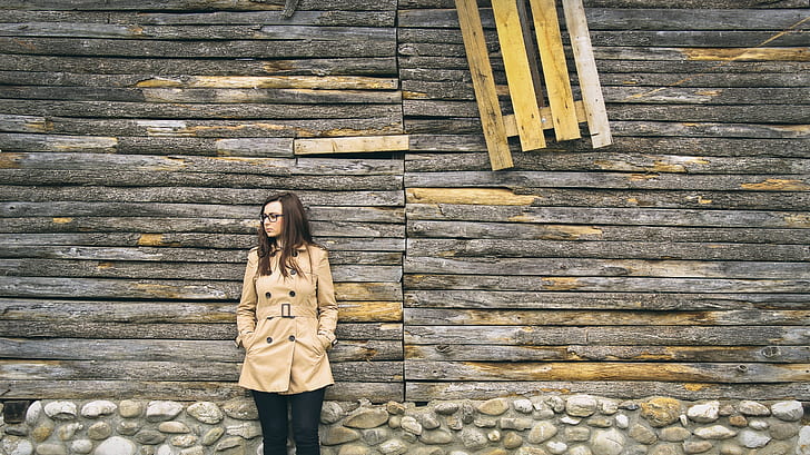 woman in beige coat leaning on brown wall