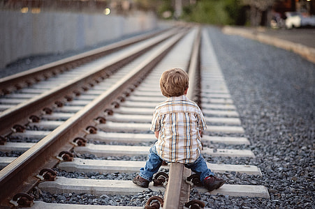 depth of field photography of boy sitting on brown metal train railway