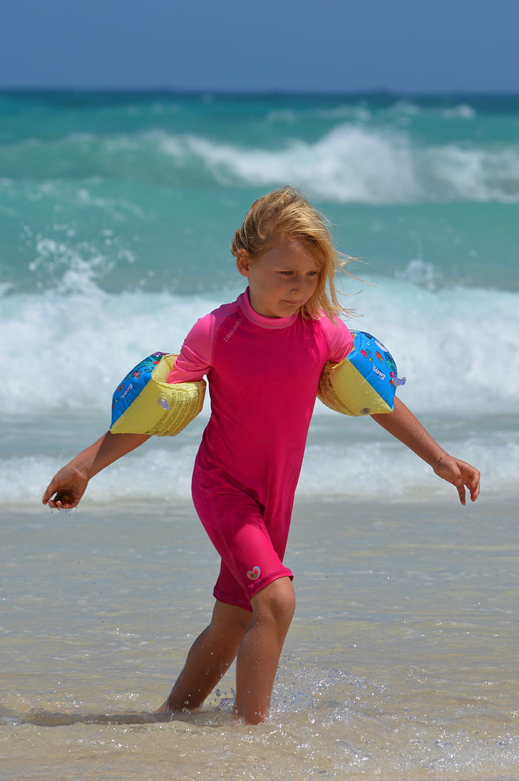 girl in pink wet suit near sea at daytime