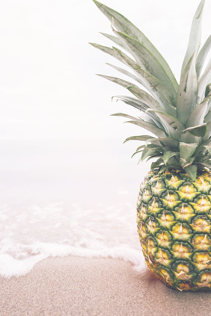 photo of pineapple on top of beach sand and water
