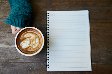 white and black ruled paper and ceramic mug filled with brown coffee