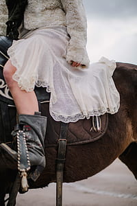 woman wearing gray fur jacket with white skirt riding on horse photo