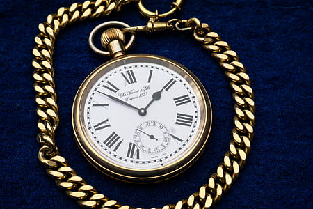 round white analog pocket watch with gold-colored frame on blue textile