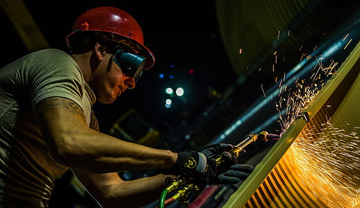 man wearing black goggles and red hard hat welding metal