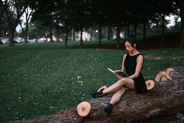 woman wearing black sleeveless dress sitting on brown tree log