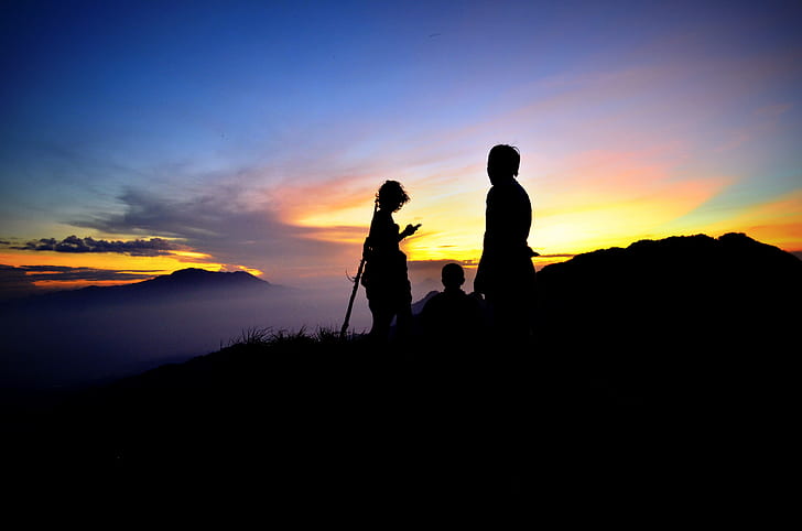 silhouette of three persons atop mountain