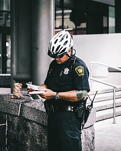 Policeman holding white notepad and black pen standing near gray concrete bench outside building