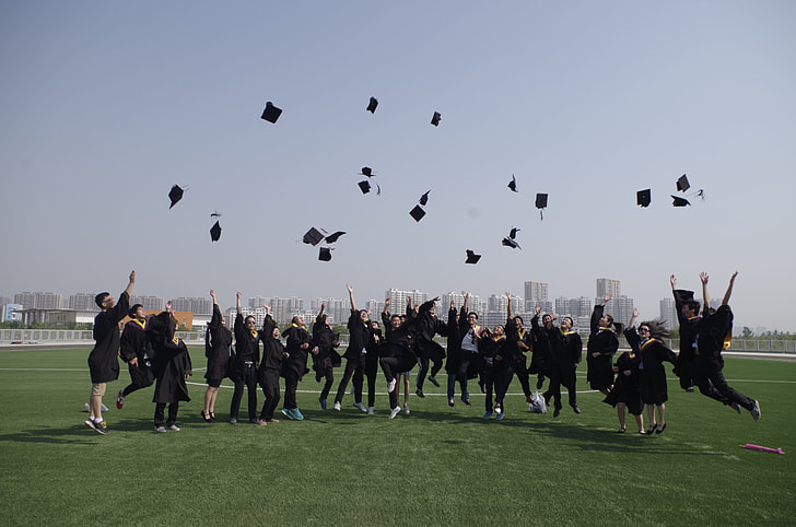 graduates throws their mortar boards up in grass field during daytime