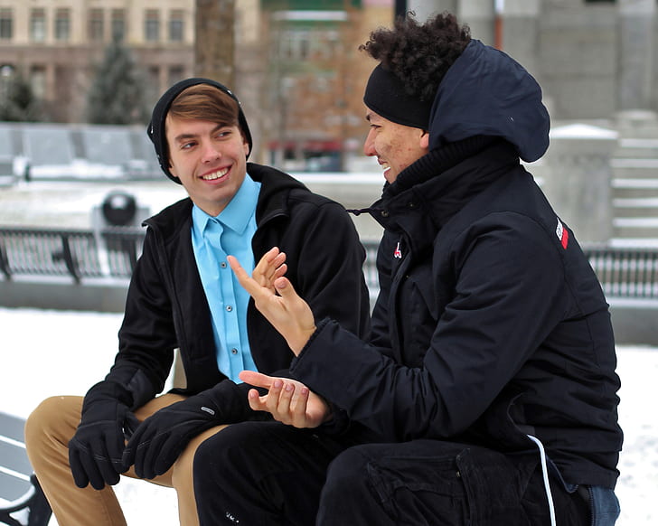 selective focus photography of two men talking on bench near snow filled area