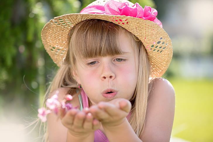 girl blowing pink petaled flowers