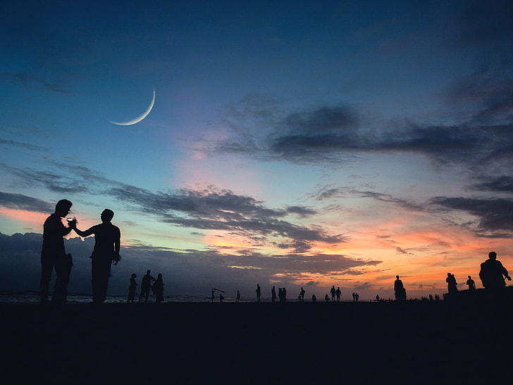 silhouette of people under crescent moon during golden hour