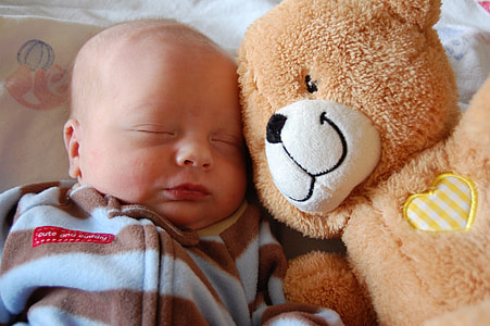 baby sleeping near brown bear plush toy