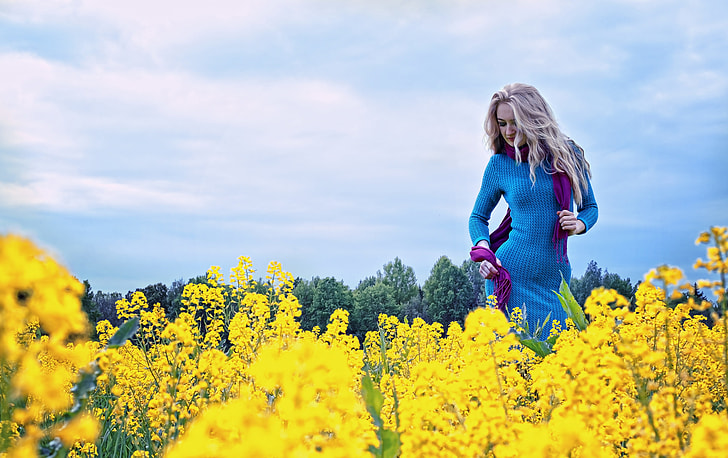 woman in blue long-sleeved dress stands on yellow petaled flower field