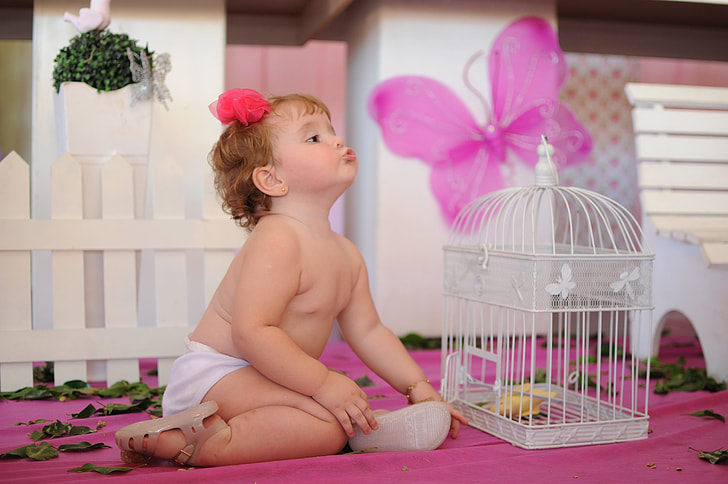 baby's white bottoms beside white metal birdcage on pink surface