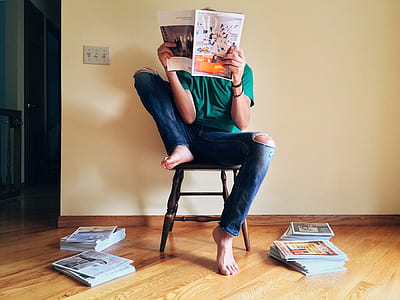 person wearing green top sitting on brown wooden chair while reading magazine