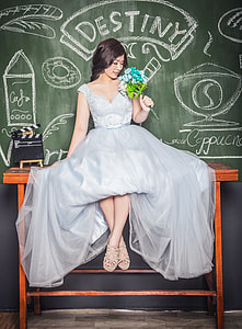 woman wearing grey satin sleeveless ball gown holding blue and white hydrangea flowers bouquet sitting on brown wooden table beside chalkboard