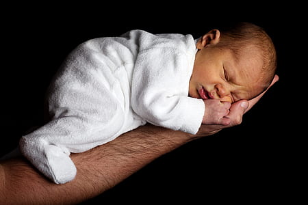 Baby in White Onesie Sleeping on Person's Hand