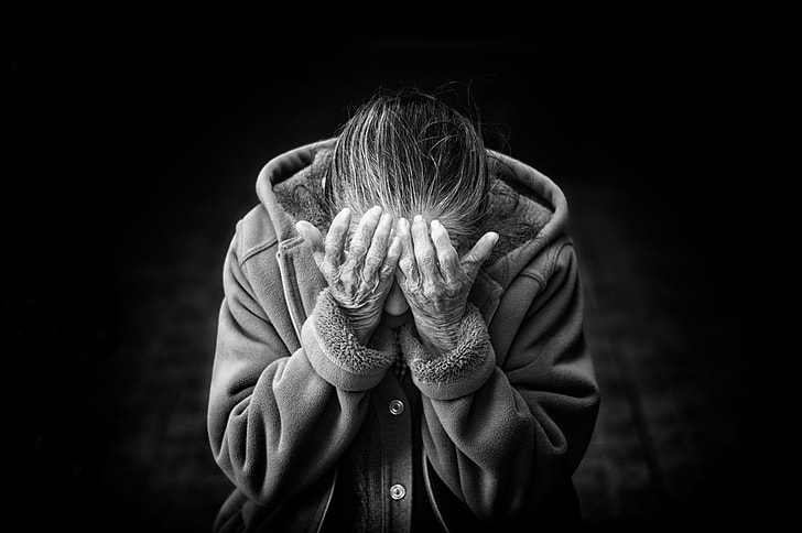 grayscale photo of person in button-up hooded jacket putting his hands in his eyes