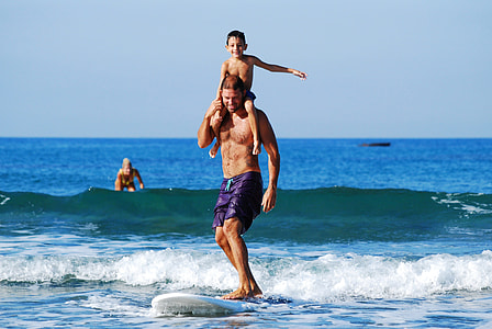 man carrying his son while riding on a white surfing board on a beach